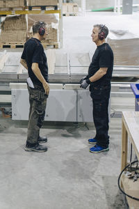 Side view of male workers talking while standing by machinery at industry