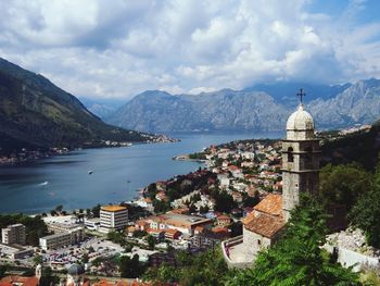 High angle view of buildings by river against mountains and cloudy sky at kotor