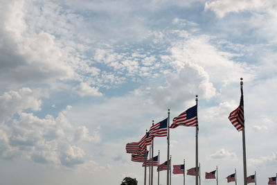 Low angle view of american flags waving against cloudy sky