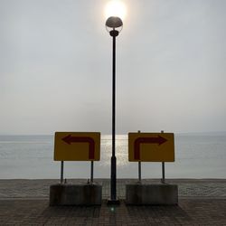 Information sign on street by sea against sky
