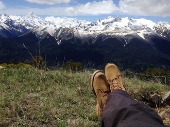 Low section of man sitting on field against snowcapped mountain