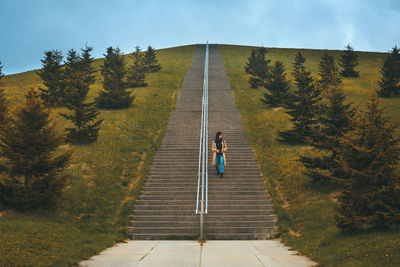 Woman moving down on steps amidst plants against sky