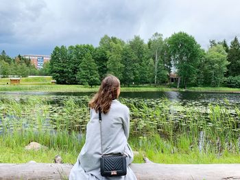 Rear view of woman standing by lake against trees