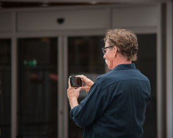 Man holding camera while standing against wall