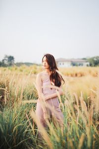 Young woman standing on grassy land against clear sky