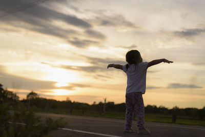 Rear view of woman standing against sky during sunset