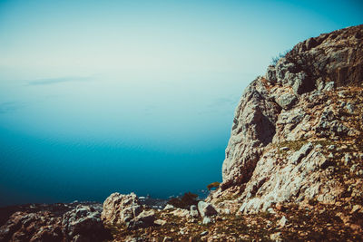 Scenic view of cliff by sea against clear blue sky