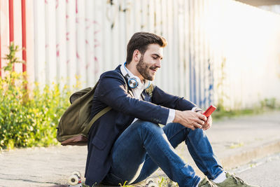 Smiling young man sitting on pavement checking cell phone