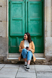 Full length of teenage girl sitting at entrance of building