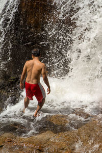 Full length of shirtless man splashing water in sea