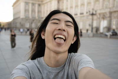 Asian young guy showing his tongue while taking selfie photo in madrid city