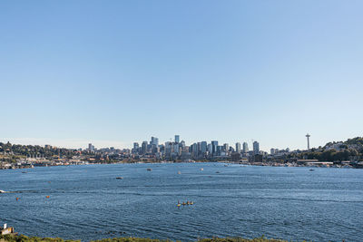 Sailboats in sea by buildings against clear blue sky