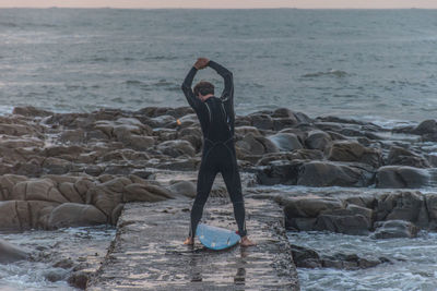 Man standing on rock at sea shore against sky