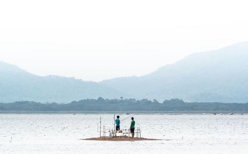 Men fishing in sea against sky