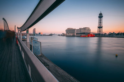 Bridge over river by buildings against sky during sunset