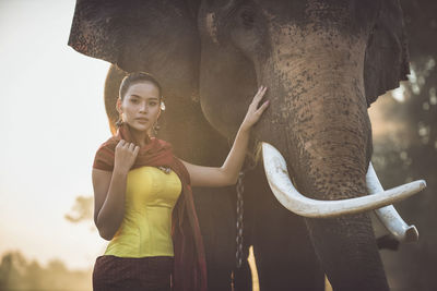 Portrait of young woman standing by elephant in forest