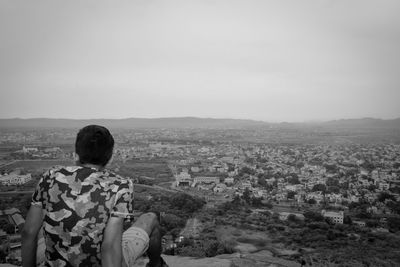 Rear view of man sitting against cityscape