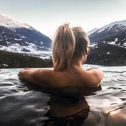 Rear view of woman swimming in lake against snowcapped mountain