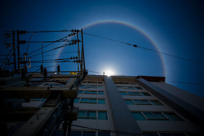 Low angle view of rainbow over buildings against blue sky