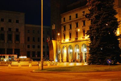 Illuminated street by buildings in city at night