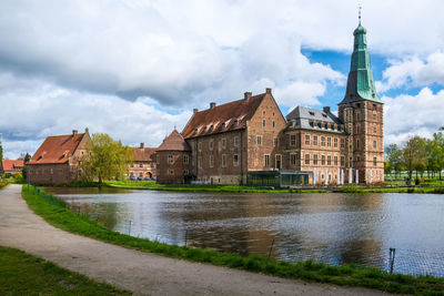 Buildings by river against cloudy sky