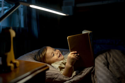 Happy boy reading book lying on bed at home