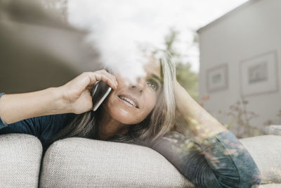 Woman on the phone sitting behind windowpane on the couch looking at distance