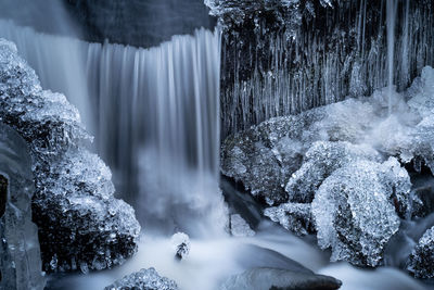 Detail of a frozen small waterfall in a forest creek with icicles