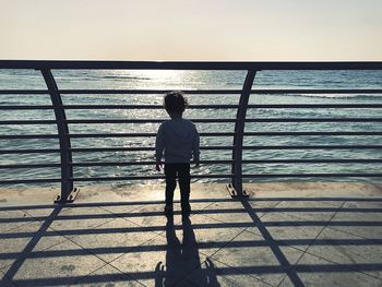 Rear view of silhouette man standing by railing against sea