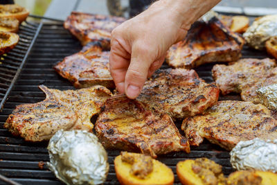 Cropped hand holding meat on barbecue grill