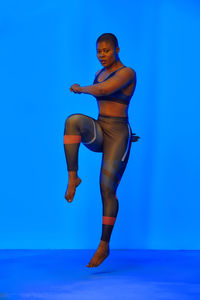 Full length of naked woman jumping against blue background