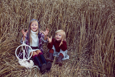 Two blonde girls in white in a dress and boots goes with a dream catcher in a wheat field