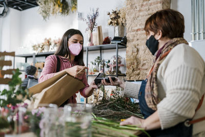 Female customer paying by credit card to florist at flower shop