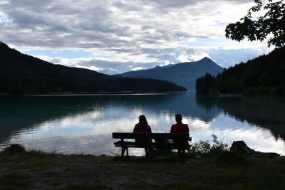 People sitting on bench by lake against sky
