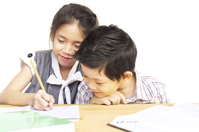 Siblings studying on table over white background