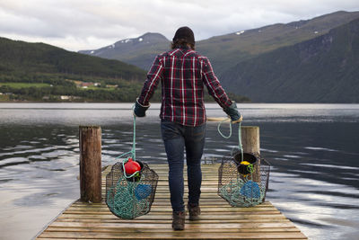 A man carries two crab pots along a dock in a fjord