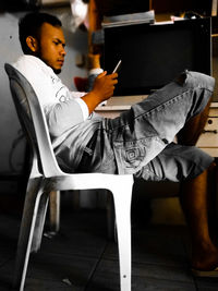 Side view of man using mobile phone while sitting on table