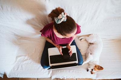 High angle view of woman using laptop while sitting on bed