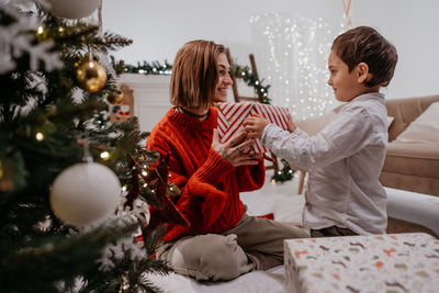 Lovely boy giving present to his mother under the christmas tree