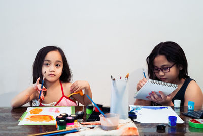 Cute little asian siblings painting a picture in home studio