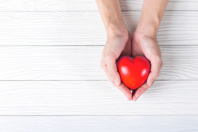 Cropped hands of person holding red heart model on white table