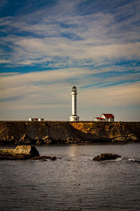 Lighthouse by sea and buildings against sky