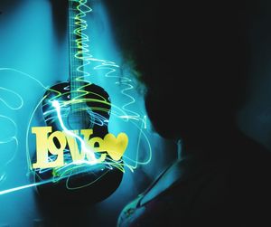 Close-up of man playing guitar against illuminated wall