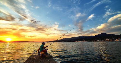 Man fishing in sea against sky during sunset