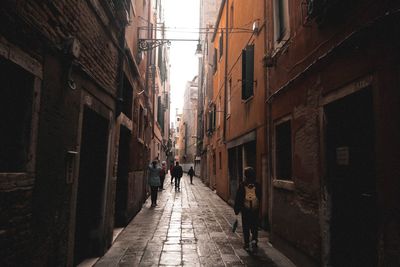 Rear view of people walking on narrow street amidst buildings