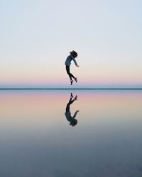 Man jumping on beach against sky during sunset