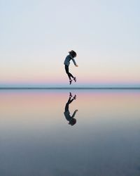 Full length of woman jumping on beach against sky during sunset