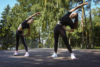 Girl in sportswear on a sunny summer day on the embankment in the park doing fitness and stretching