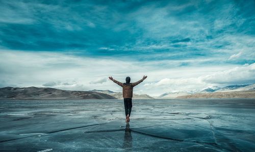 Man with arms outstretched walking on frozen sea against sky
