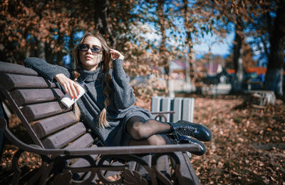 Portrait of young woman sitting on bench in park